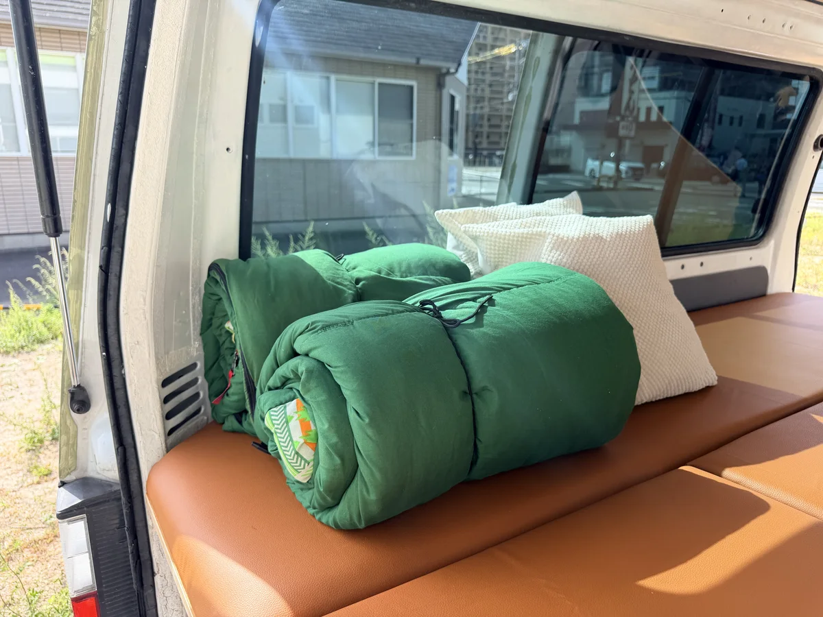 Two green sleeping bags and pillows on the bed of a Bongo campervan with the back door open